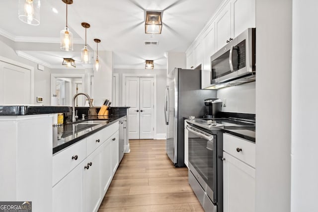 kitchen featuring decorative light fixtures, sink, light wood-type flooring, appliances with stainless steel finishes, and white cabinets