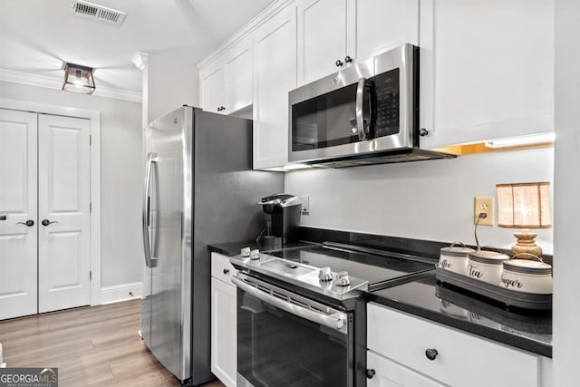 kitchen featuring white cabinets, appliances with stainless steel finishes, dark stone countertops, light wood-type flooring, and crown molding