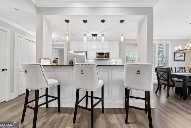 kitchen featuring decorative light fixtures, a breakfast bar, white cabinetry, and stainless steel appliances