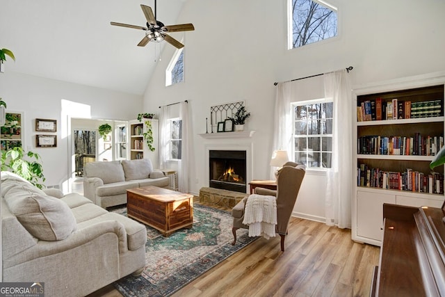 living room with ceiling fan, a high ceiling, and light hardwood / wood-style flooring