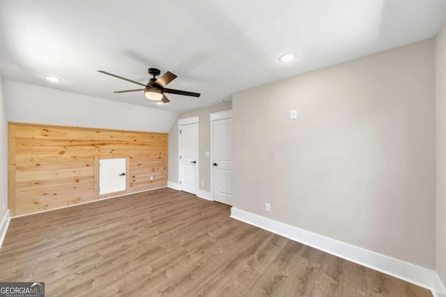 empty room with ceiling fan, vaulted ceiling, wooden walls, and hardwood / wood-style flooring