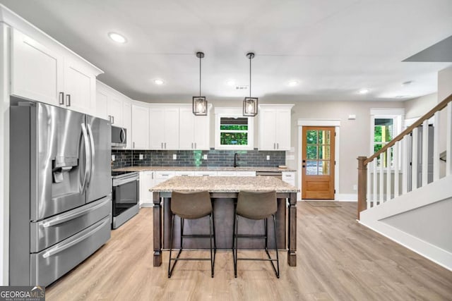 kitchen with hanging light fixtures, stainless steel appliances, white cabinetry, and a kitchen island