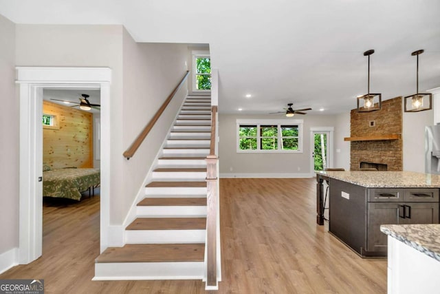 staircase featuring ceiling fan, hardwood / wood-style flooring, and a stone fireplace