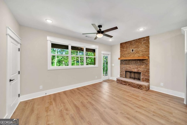 unfurnished living room featuring light hardwood / wood-style floors, ceiling fan, and a stone fireplace