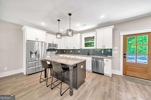 kitchen featuring decorative light fixtures, white cabinets, stainless steel appliances, and a kitchen island