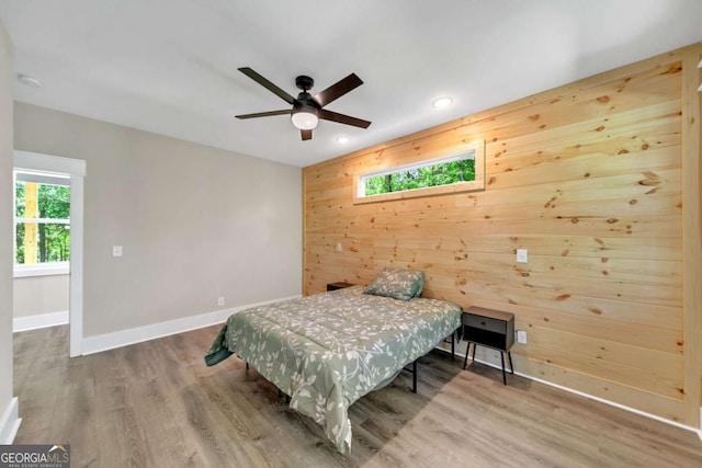 bedroom with ceiling fan, hardwood / wood-style floors, and wooden walls