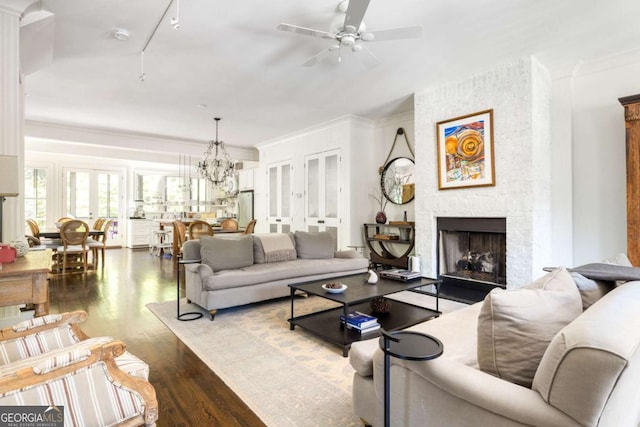 living room featuring a brick fireplace, hardwood / wood-style floors, track lighting, ornamental molding, and ceiling fan with notable chandelier