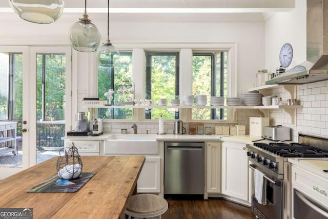 kitchen with pendant lighting, appliances with stainless steel finishes, white cabinetry, wall chimney range hood, and butcher block countertops