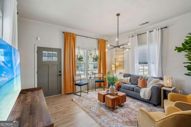 living room with light hardwood / wood-style flooring, ornamental molding, and a notable chandelier