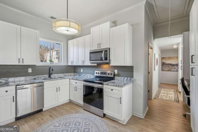 kitchen with pendant lighting, appliances with stainless steel finishes, white cabinetry, sink, and light hardwood / wood-style flooring