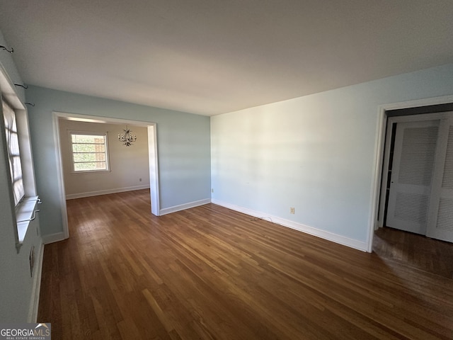 spare room with dark wood-type flooring and a chandelier