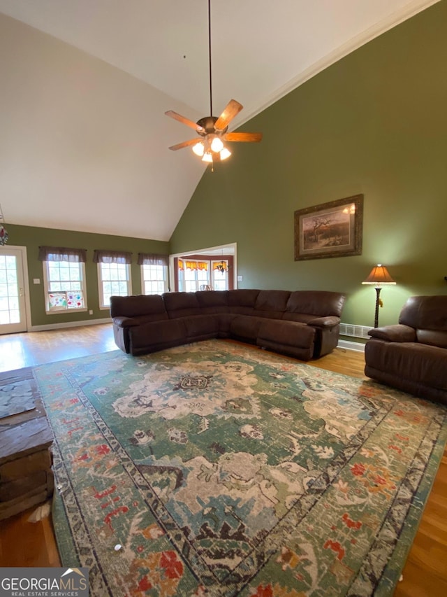 living room featuring wood-type flooring, crown molding, ceiling fan, and high vaulted ceiling