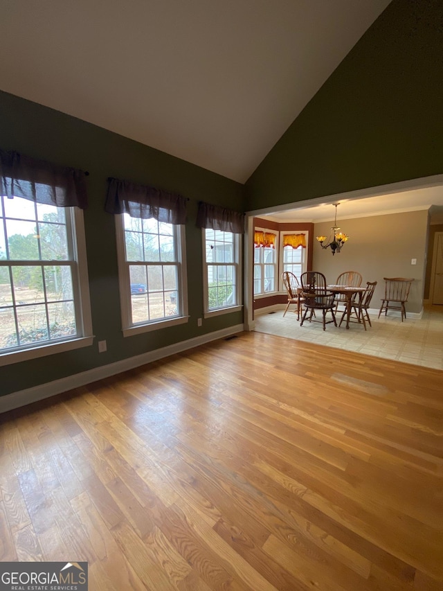 unfurnished living room with high vaulted ceiling, a notable chandelier, and light wood-type flooring