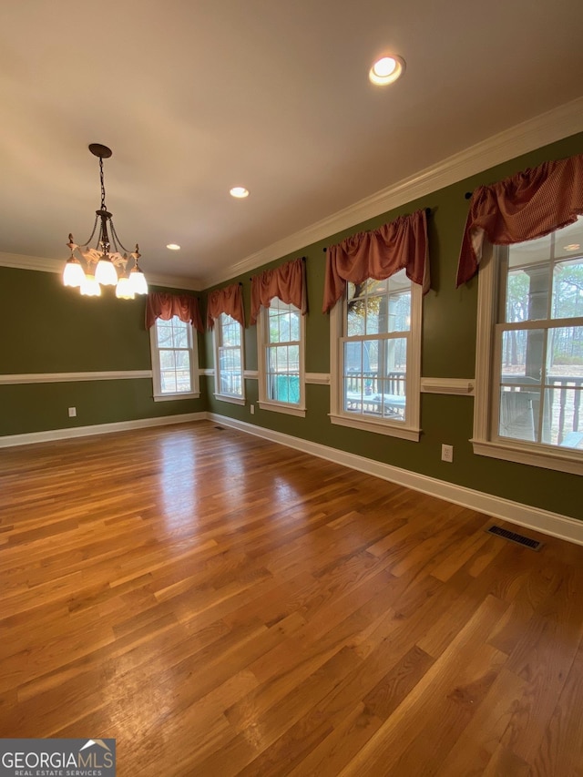 unfurnished dining area featuring wood-type flooring, ornamental molding, and an inviting chandelier