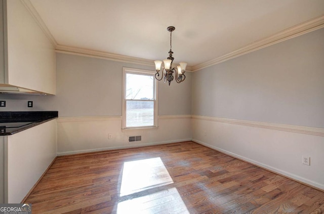 unfurnished dining area featuring an inviting chandelier, ornamental molding, and light hardwood / wood-style floors