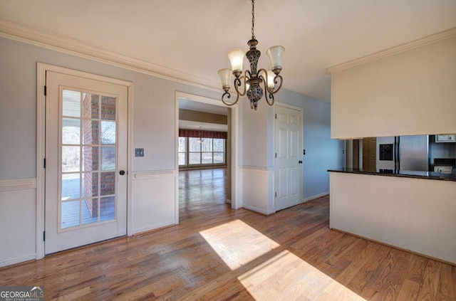 unfurnished dining area featuring light hardwood / wood-style flooring, crown molding, and a notable chandelier