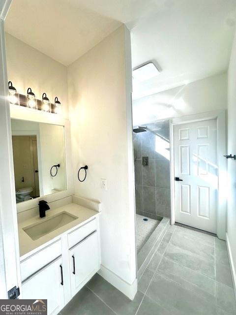 bathroom featuring vanity, toilet, tile patterned flooring, and tiled shower