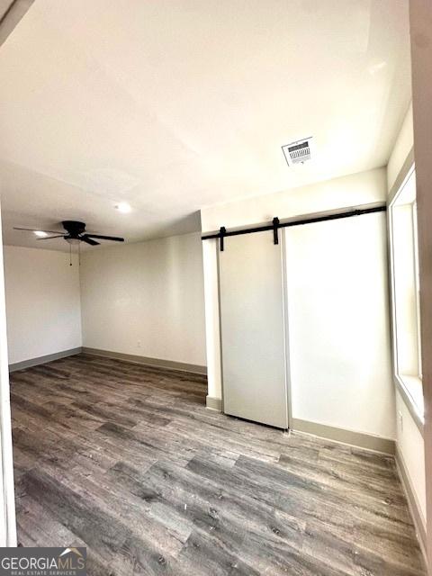 empty room featuring ceiling fan, a barn door, and wood-type flooring