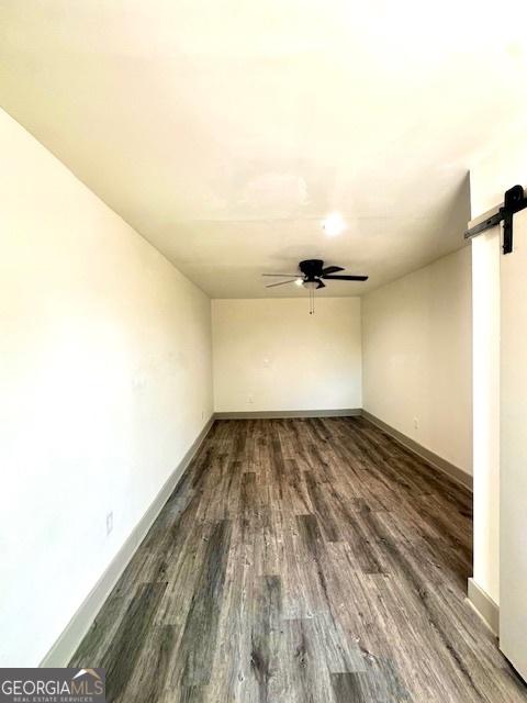 spare room with ceiling fan, a barn door, and dark hardwood / wood-style floors