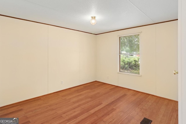 unfurnished room featuring a textured ceiling, light hardwood / wood-style flooring, and ornamental molding