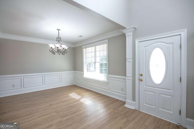 foyer featuring light wood-type flooring, a notable chandelier, crown molding, and decorative columns