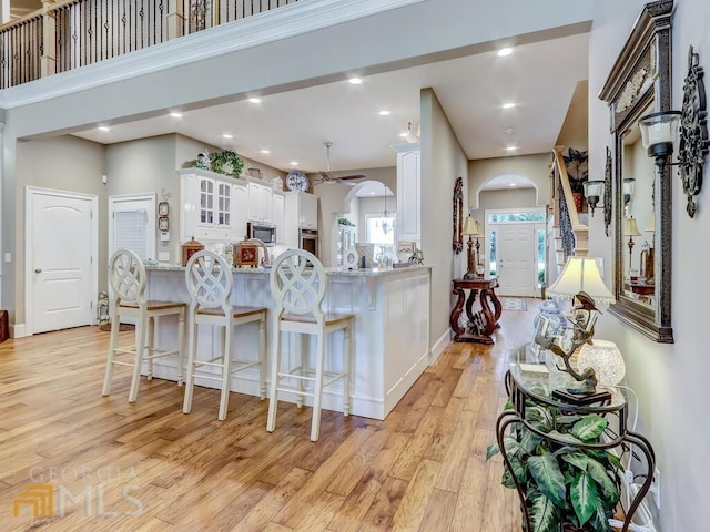 kitchen with kitchen peninsula, a high ceiling, white cabinetry, light hardwood / wood-style flooring, and appliances with stainless steel finishes