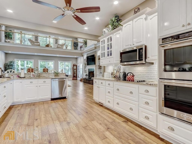 kitchen with light hardwood / wood-style floors, decorative backsplash, white cabinetry, light stone countertops, and appliances with stainless steel finishes