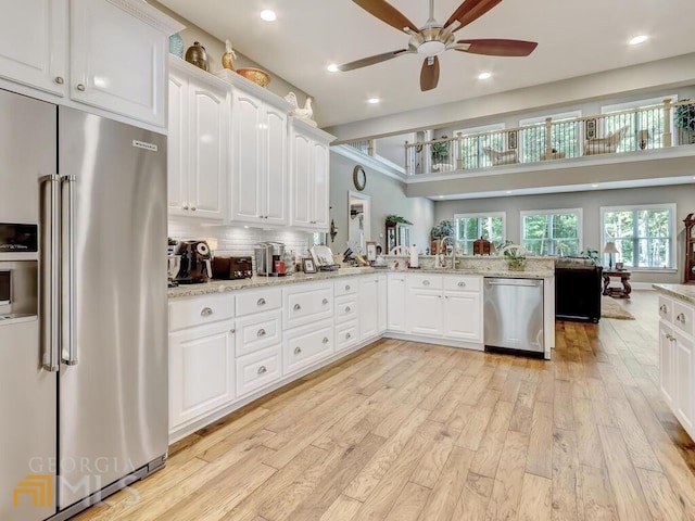 kitchen with white cabinetry, light hardwood / wood-style floors, appliances with stainless steel finishes, decorative backsplash, and light stone countertops