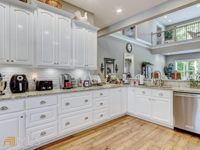 kitchen featuring light stone countertops, white cabinets, dishwasher, decorative backsplash, and light wood-type flooring