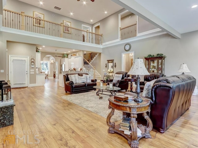 living room featuring ceiling fan, light wood-type flooring, a towering ceiling, and beamed ceiling