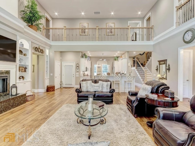 living room featuring light hardwood / wood-style floors, a fireplace, a high ceiling, and built in shelves