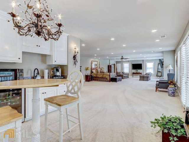 kitchen with white cabinetry, light colored carpet, beverage cooler, ceiling fan with notable chandelier, and a breakfast bar