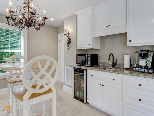 kitchen featuring light stone counters, sink, white cabinetry, and wine cooler