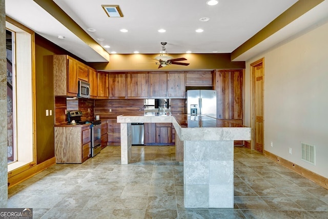 kitchen with ceiling fan, tasteful backsplash, stainless steel appliances, and a center island