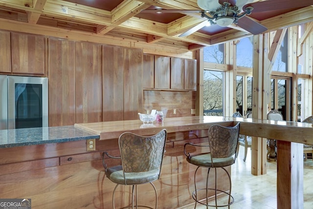 bar featuring stainless steel fridge, coffered ceiling, wooden walls, dark stone counters, and beamed ceiling