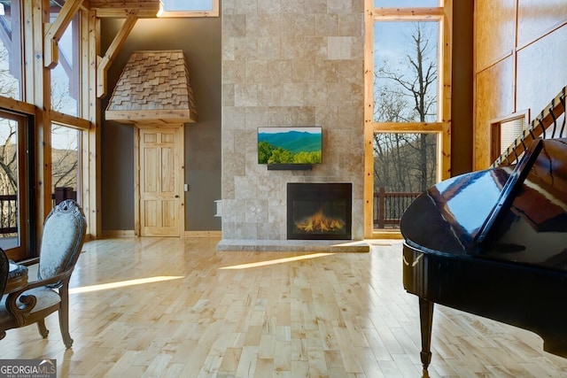 interior space featuring a high ceiling, light hardwood / wood-style flooring, a tiled fireplace, and a healthy amount of sunlight