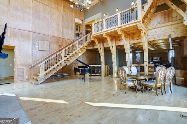 unfurnished dining area with a high ceiling, hardwood / wood-style floors, a notable chandelier, and wooden walls