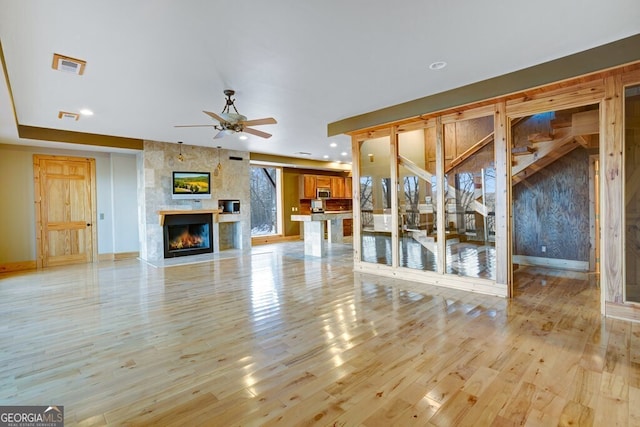 unfurnished living room featuring ceiling fan, light hardwood / wood-style floors, and a large fireplace