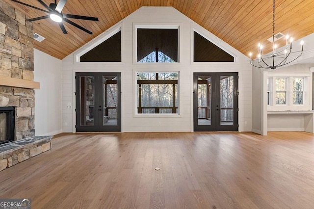 unfurnished living room with ceiling fan with notable chandelier, hardwood / wood-style floors, a stone fireplace, french doors, and wooden ceiling