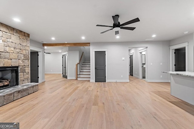 unfurnished living room with ceiling fan, a stone fireplace, and light hardwood / wood-style flooring