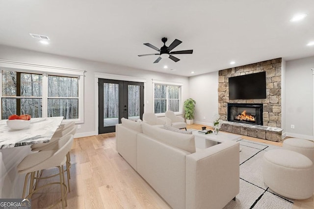 living room with ceiling fan, french doors, light wood-type flooring, and a stone fireplace