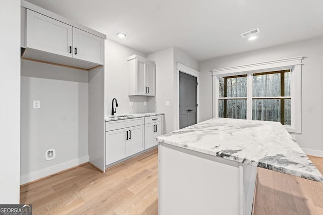 kitchen featuring light hardwood / wood-style floors, light stone countertops, white cabinets, and sink