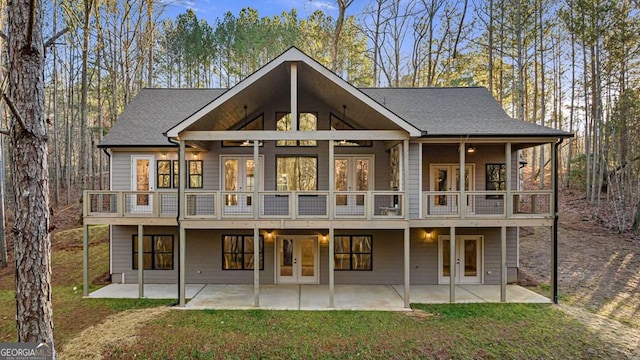 rear view of house with a balcony, french doors, a lawn, and a patio