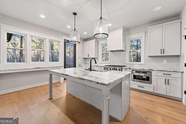 kitchen with decorative light fixtures, a center island with sink, white cabinetry, light stone countertops, and stainless steel appliances