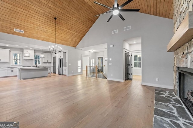 unfurnished living room featuring light hardwood / wood-style flooring, wood ceiling, a stone fireplace, high vaulted ceiling, and ceiling fan with notable chandelier