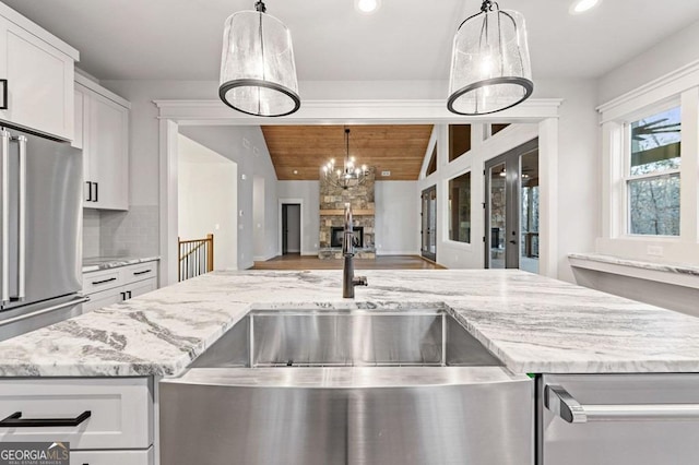 kitchen with tasteful backsplash, high quality fridge, wood ceiling, a stone fireplace, and white cabinets