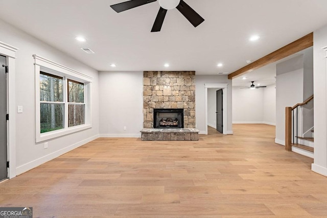 unfurnished living room with a fireplace, beamed ceiling, ceiling fan, and light wood-type flooring