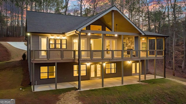 back house at dusk with a balcony and a patio