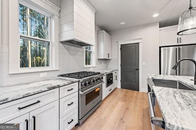 kitchen with light stone counters, white cabinetry, hanging light fixtures, and high end appliances