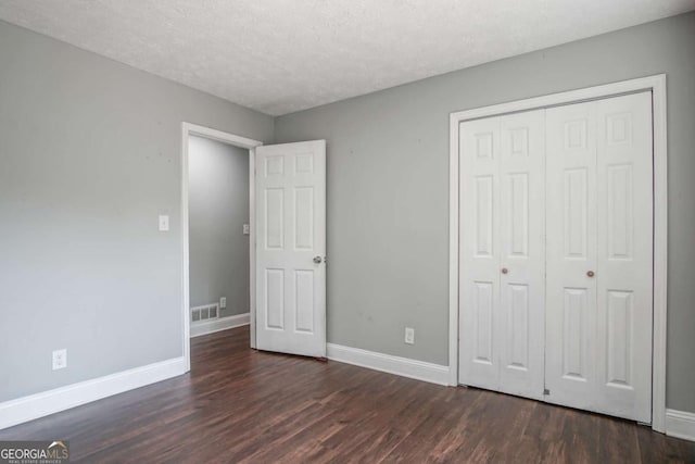 unfurnished bedroom with a textured ceiling, dark wood-type flooring, and a closet